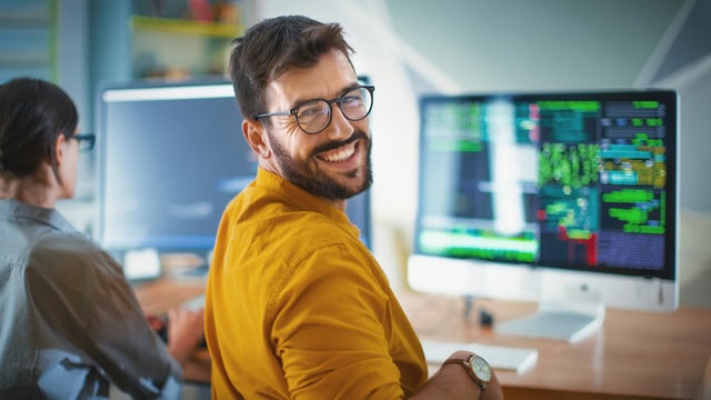 Lächelnder IT-Experte vor Monitor mit IT-Monitoring-Dashboard – Symbolbild für professionelle Unterstützung und Expertenwissen im IT-Monitoring mit USU.