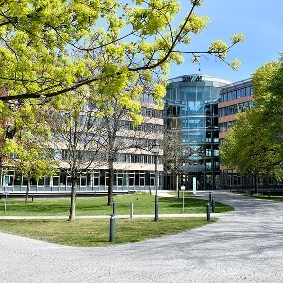 Vue extérieure du bâtiment de Stadtwerke München (SWM), entouré d'une nature verdoyante. SWM est un client de la solution de surveillance informatique d'USU.