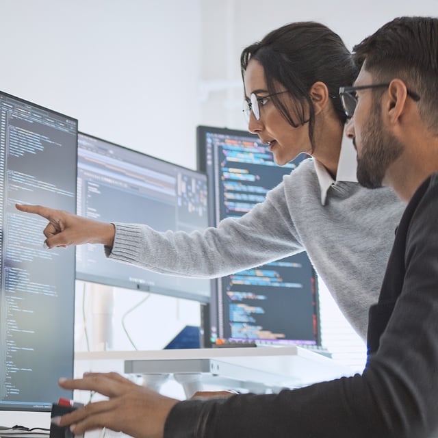 Deux informaticiens analysent ensemble le code source sur plusieurs moniteurs afin de gérer activement les risques informatiques.