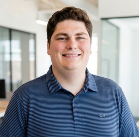 Portrait of a smiling man wearing a navy striped polo shirt in a bright office setting