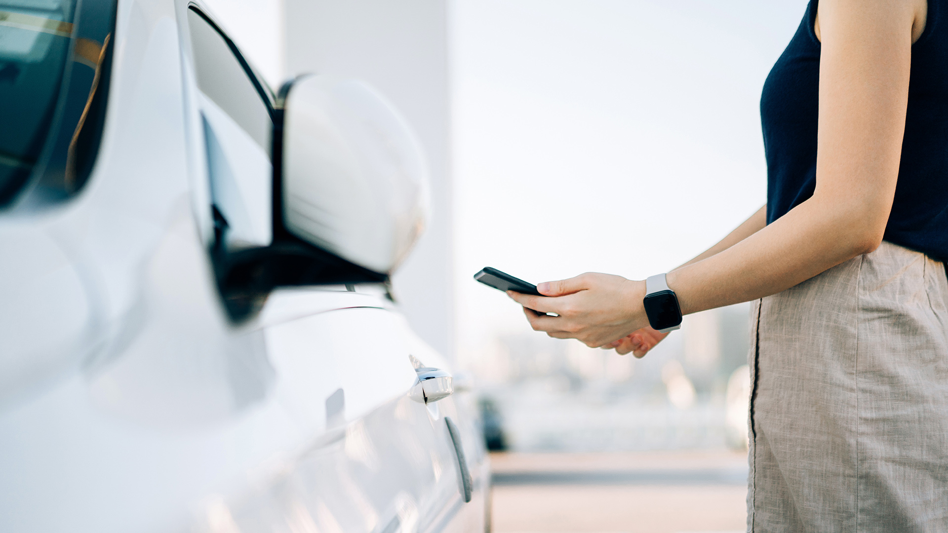 Frau mit Smartphone neben Auto